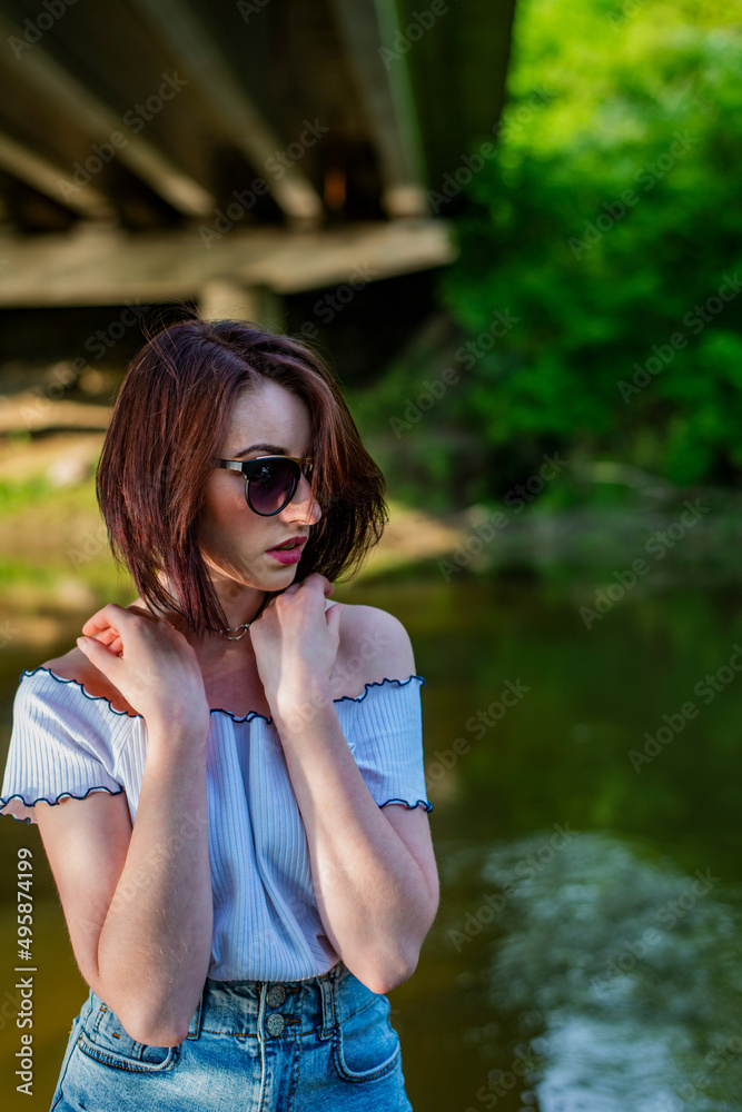 Red haired young girl wrapped in orange blanket posing near the swamp or lake with duckweed