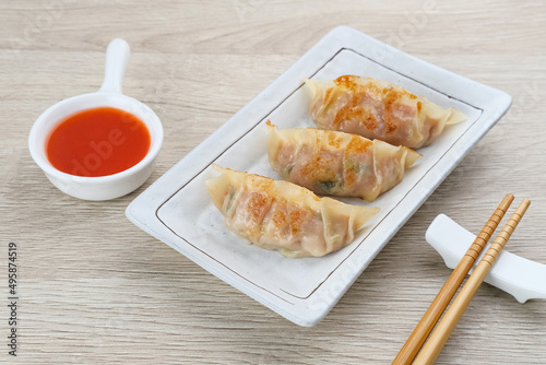 Korean Mandu Dumplings, made from flour dough and filled with seasoned chicken. Served on a plate with chili sauce
