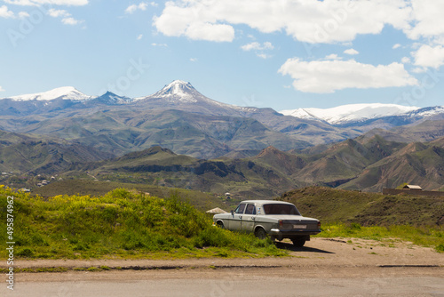 An old Soviet car stands on the roadside against the backdrop of snow-capped mountain peaks. Armenia