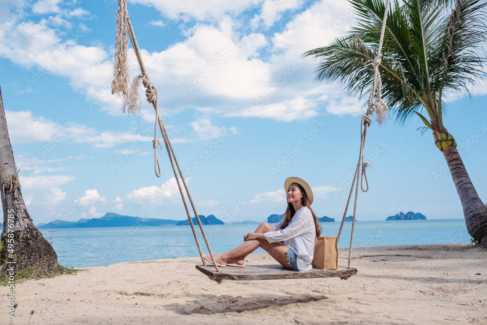 Portrait image of a beautiful young asian woman sitting on wooden swing by the sea