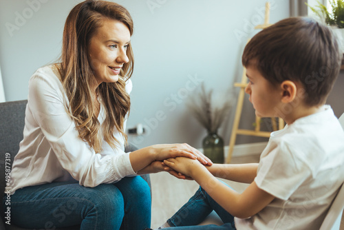 Shot of a little boy talking to a psychologist. Attentive and sympathetic woman psychologist listens to little boy. Notes to himself in clipboard. Mental health.