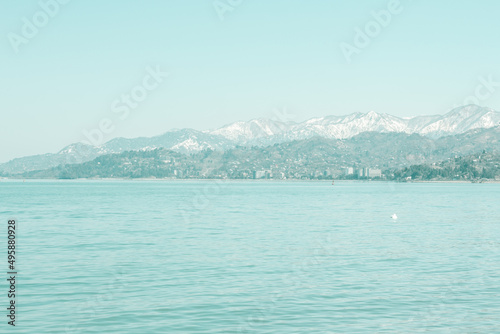 Calm blue sea wallpaper with snowy mountain peaks at a distance. Fresh spring background in blue colors. 