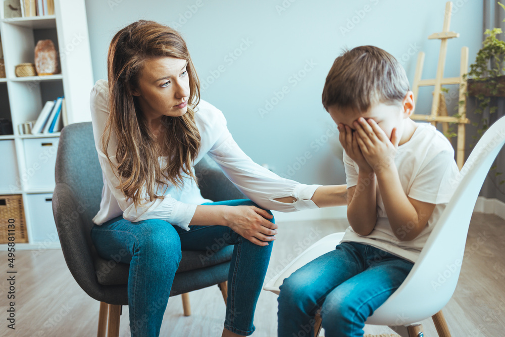 Psychologist touching shoulder of frustrated little boy while trying to help him. Young supported adoption counselor showing a drawing of house to sad pensive little boy waiting for new loving family Psychologist touching shoulder of frustrated little boy while trying to help him. Young supported adoption counselor showing a drawing of house to sad pensive little boy waiting for new loving family