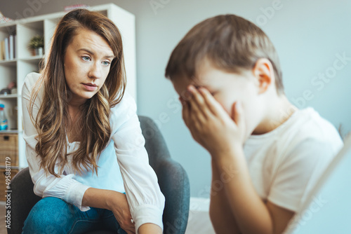 Parenthood and child development, young worried mother comforting little son crying at home. Worried mother comforting crying son. Young boy having therapy with a child psychologist photo