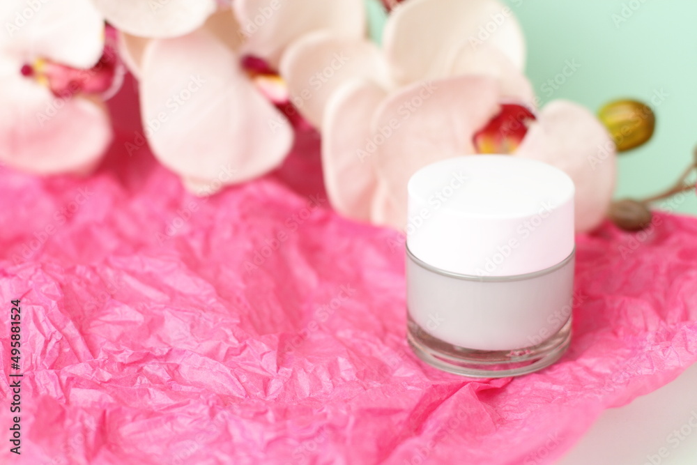 Green light cream in crystal jar with orchid flower on pink paper Green light cream in crystal jar with orchid flower on pink paper