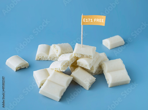 Heap of white chocolate cubes with the sign of a dangerous additive e171 on a blue background photo