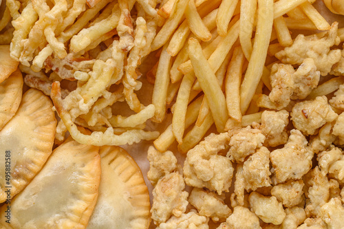 Close-up fragment of a multiple french fries potato chips and fried pies as a food backdrop composition