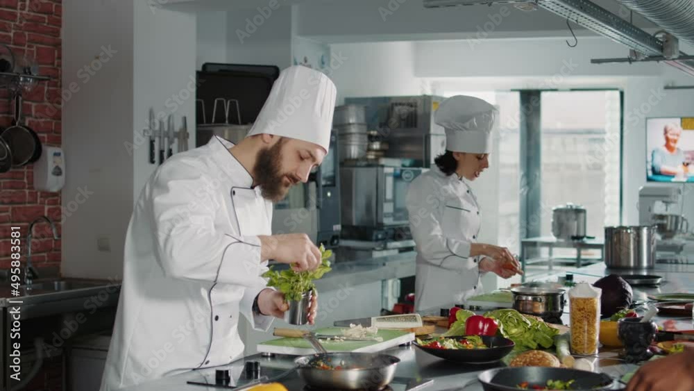 Young man adding rosemary leaves in delicious cooked dish, making gourmet meal with celery and organic vegetables. Professional chef in uniform using natural plant to prepare healthy food. Young man adding rosemary leaves in delicious cooked dish, making gourmet meal with celery and organic vegetables. Professional chef in uniform using natural plant to prepare healthy food.