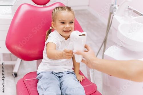 Little girl smiling on a visit to the dentist holding a tooth model at the dental clinic