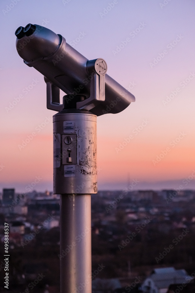 Observation deck and binoculars with a view of the city. Coin operated telescope binocular for sightseeing. Sunset above the european city from the viewing point