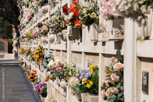 Italian wall cemetery with tombstones and artificial flowers on a sunny summer day in Venice, Italy, Island of San Michele. Commemoration of the dead, deaths of pandemic.