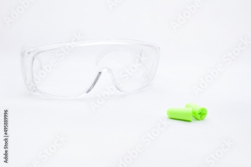Protective equipment - earplugs against noise and plastic transparent protective work goggles isolated on white background. Hearing protection. Necessity in a noisy environment.