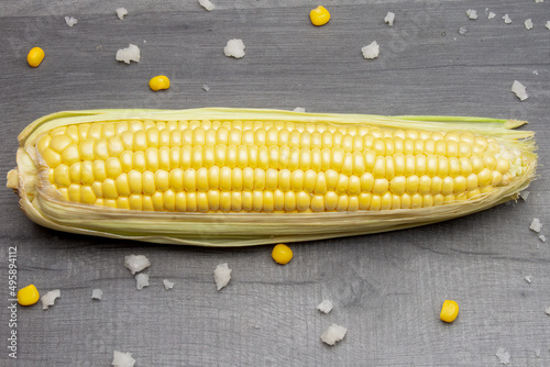 A cob of fresh sweet corn lying on a gray table surrounded by salt.
