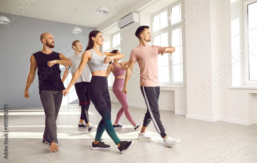 Fototapeta Naklejka Na Ścianę i Meble -  Group of fit young people doing physical exercises with a fitness instructor at the gym. Team of happy men and women enjoying an aerobics or sports dance workout class with a professional teacher