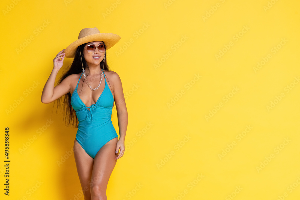 Beautiful asian girl in a swimsuit and and the hat on a yellow background Beautiful asian girl in a swimsuit and and the hat on a yellow background