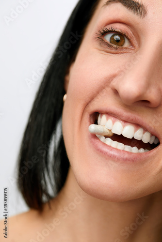 Pretty young woman with a pill in her teeth  isolated against white background. Taking supplement pill into her Mouth. Healthy Eating And Diet Nutrition Concepts.