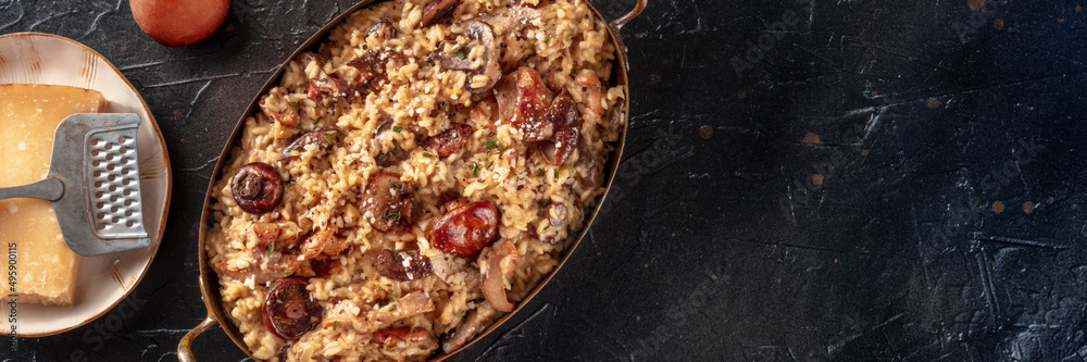 Risotto ai funghi panorama, mushroom rice with cheese, shot from above on a black background with copy space