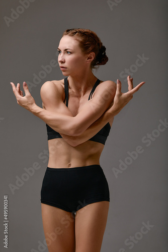 Young attractive gymnastic woman exercise, working out, wearing black sportswear, cool urban style, full length, grey studio background, side view