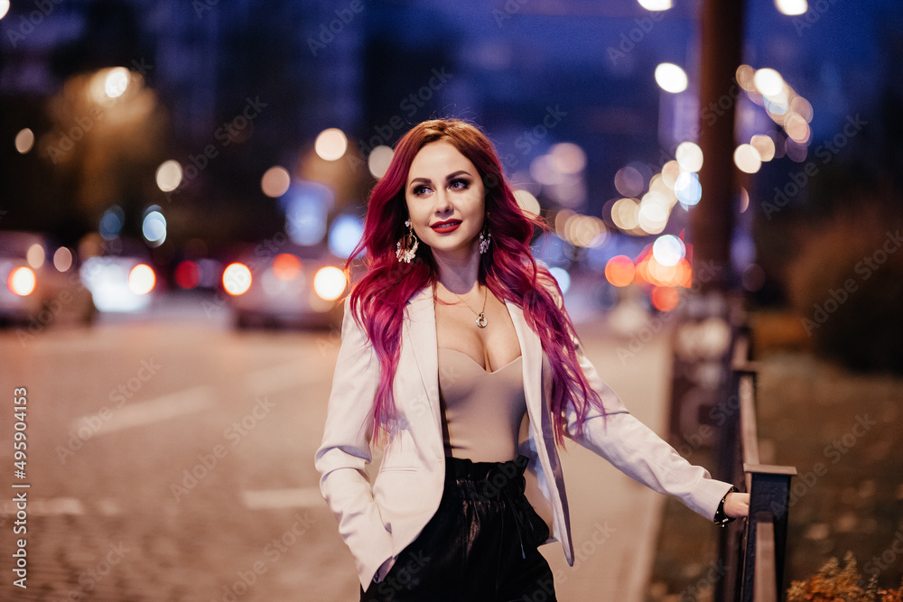 woman with pink hair looking at camera in the city at night while it snows