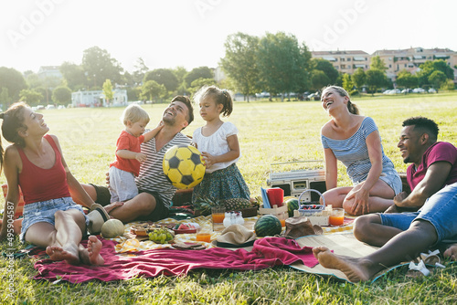 Happy families having fun doing picnic at park outdoor in summer vacation - Focus on african man face