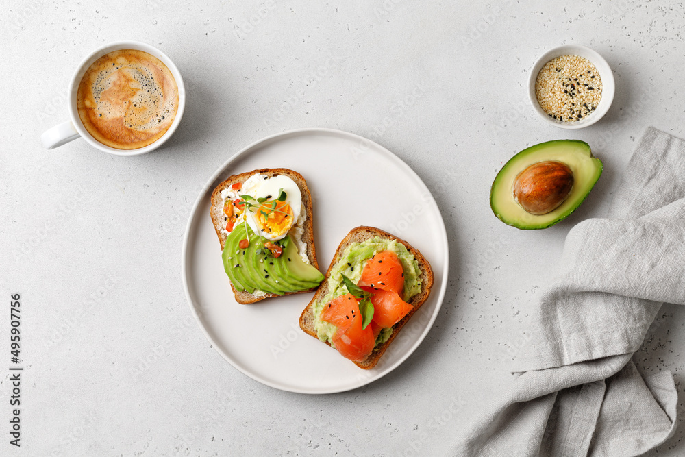 Two avocado sandwiches with salmon, eggs, basil, micro greens. White plate and cup of coffee