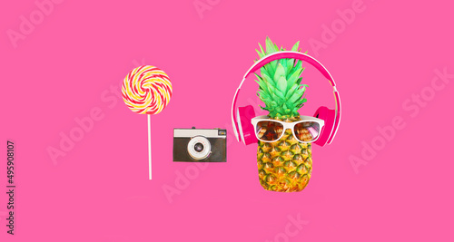 Fashion pineapple with headphones, sunglasses, lollipop caramel on stick and film camera on colorful pink background