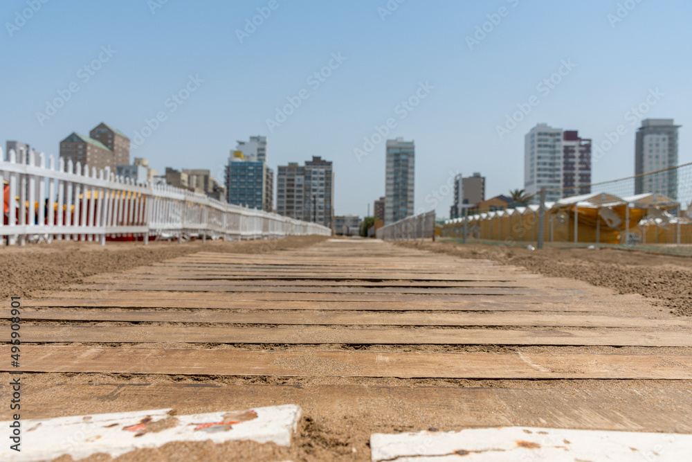Selective focus of a wooden pathway on the beach with city buildings in the background