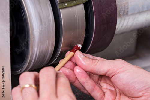 craftsman rolling a wooden stick under a metal lap with the white gemstone on it during cutting process on cabochon machine photo