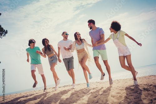 Photo of positive tourist people walk hold hands walk jump wear sunglass casual clothes nature summer seaside beach