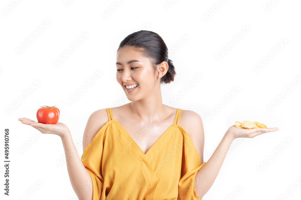 Attractive beautiful young asian woman in a pretty yellow dress choosing between fresh tomato and potato chips isolated on white background. Healthy diet food concept. Attractive beautiful young asian woman in a pretty yellow dress choosing between fresh tomato and potato chips isolated on white background. Healthy diet food concept.