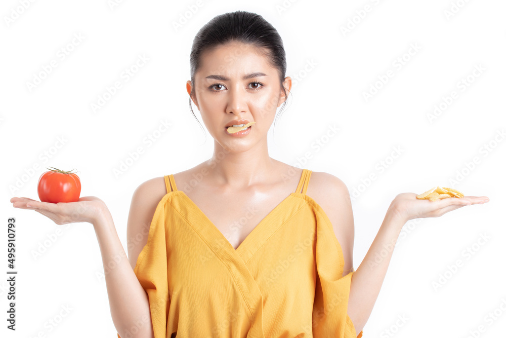 Attractive beautiful young asian woman in a pretty yellow dress choosing between fresh tomato and potato chips isolated on white background. Healthy diet food concept. Attractive beautiful young asian woman in a pretty yellow dress choosing between fresh tomato and potato chips isolated on white background. Healthy diet food concept.