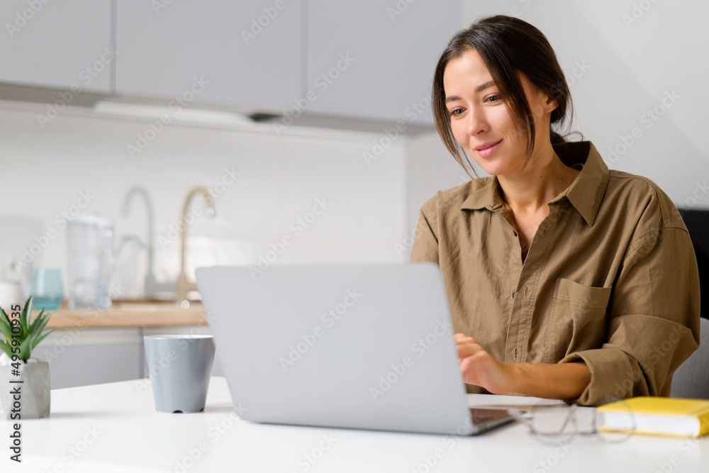 Female freelancer daydreaming with a cup of morning coffee, smiling woman sitting at the table with laptop, looks at the screen, waiting for inspiration or new ideas Female freelancer daydreaming with a cup of morning coffee, smiling woman sitting at the table with laptop, looks at the screen, waiting for inspiration or new ideas