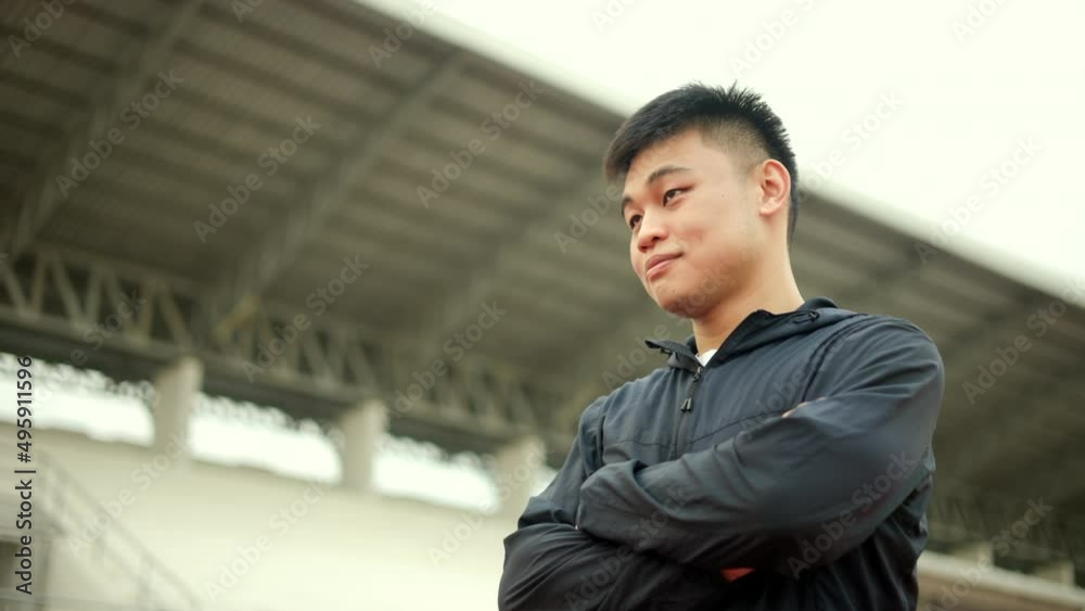 Young handsome asian man wearing sportswear dark blue jacket standing post at track stadium running outdoor. Portraits of Chinese man jogging on the road. Training athlete outdoor concept. Young handsome asian man wearing sportswear dark blue jacket standing post at track stadium running outdoor. Portraits of Chinese man jogging on the road. Training athlete outdoor concept.