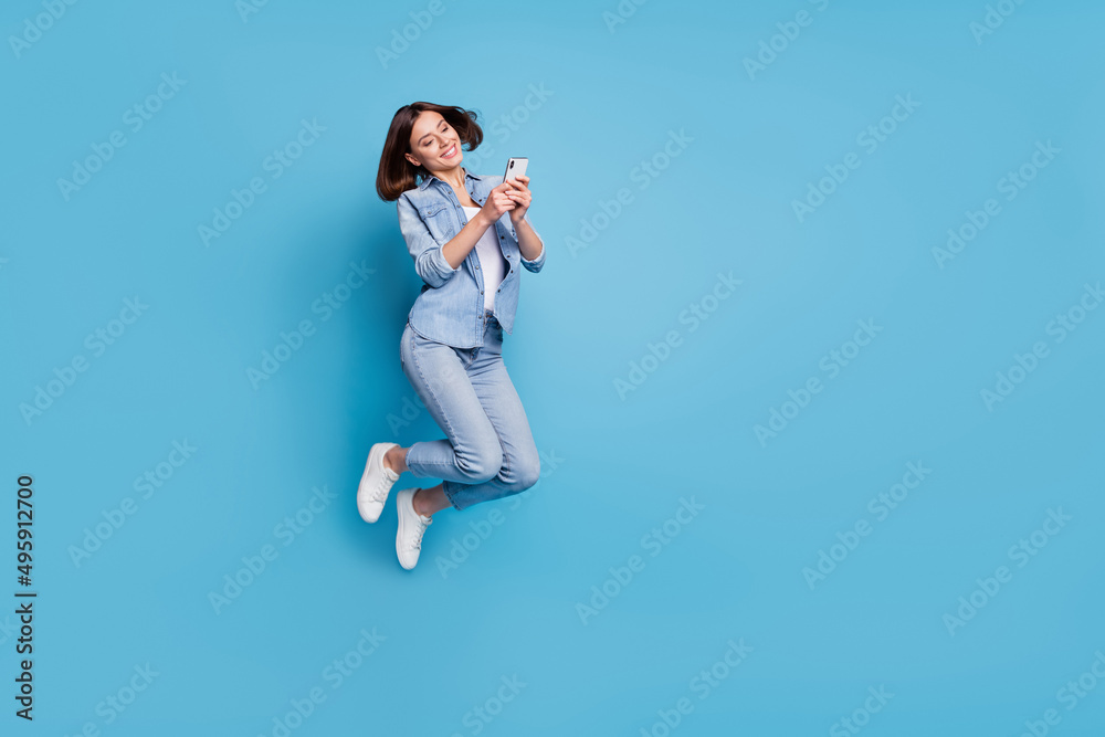 Photo of pretty sweet lady dressed denim shirt jumping typing gadget empty space isolated blue color background Photo of pretty sweet lady dressed denim shirt jumping typing gadget empty space isolated blue color background