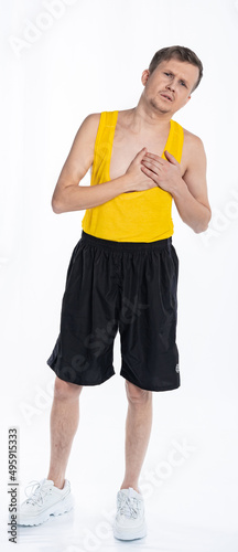 Tired sick man with a thin body, an athlete in black shorts and a yellow t-shirt, feels a lot of pain, spasm in the heart on a white background.