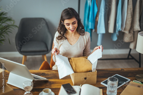 Фотография Excited caucasian young woman sit on chair at home unpack cardboard box shopping