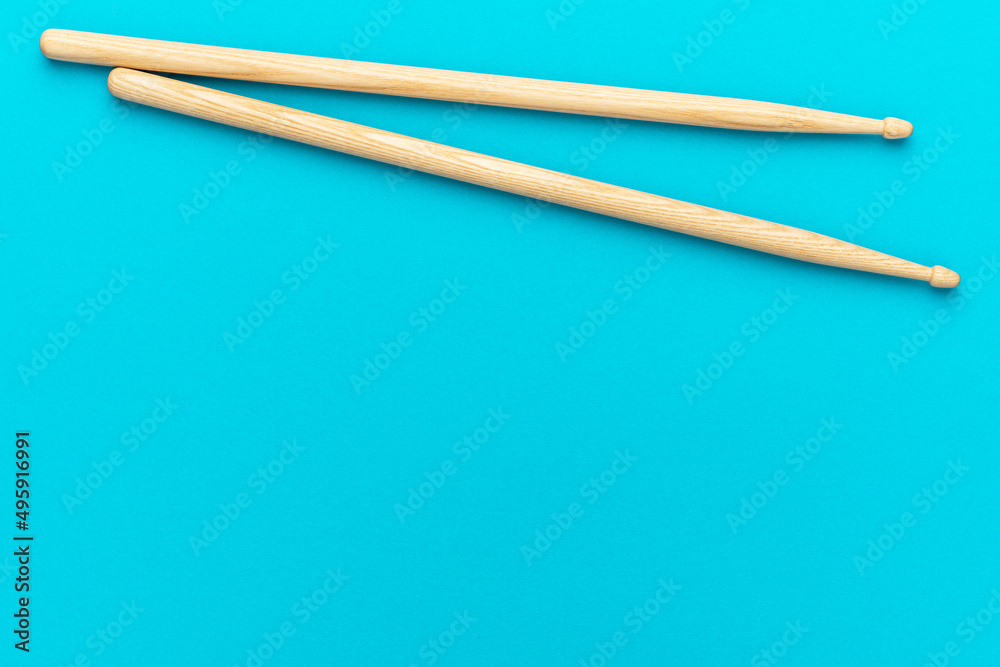 Minimalist photo of pair of wooden drumsticks on turquoise blue background. Flat lay top-down composition of drumsticks with copy space.