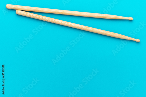 Minimalist photo of pair of wooden drumsticks on turquoise blue background. Flat lay top-down composition of drumsticks with copy space.