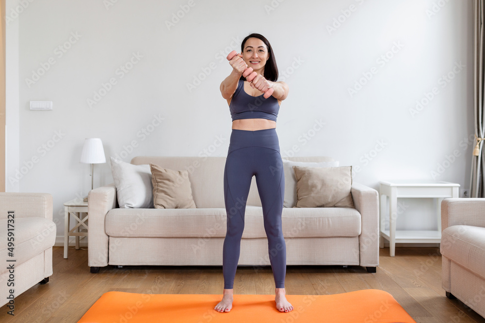 Asian woman exercise with dumbbells at home. Happy female doing arm workout using dumbbells Asian woman exercise with dumbbells at home. Happy female doing arm workout using dumbbells