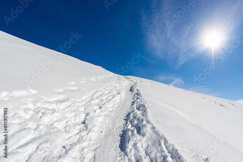 Beautiful winter landscape with powder snow and footprints against a clear blue sky and sunbeams. Lessinia Plateau Regional Natural Park (Altopiano della Lessinia), Verona Province, Veneto, Italy.