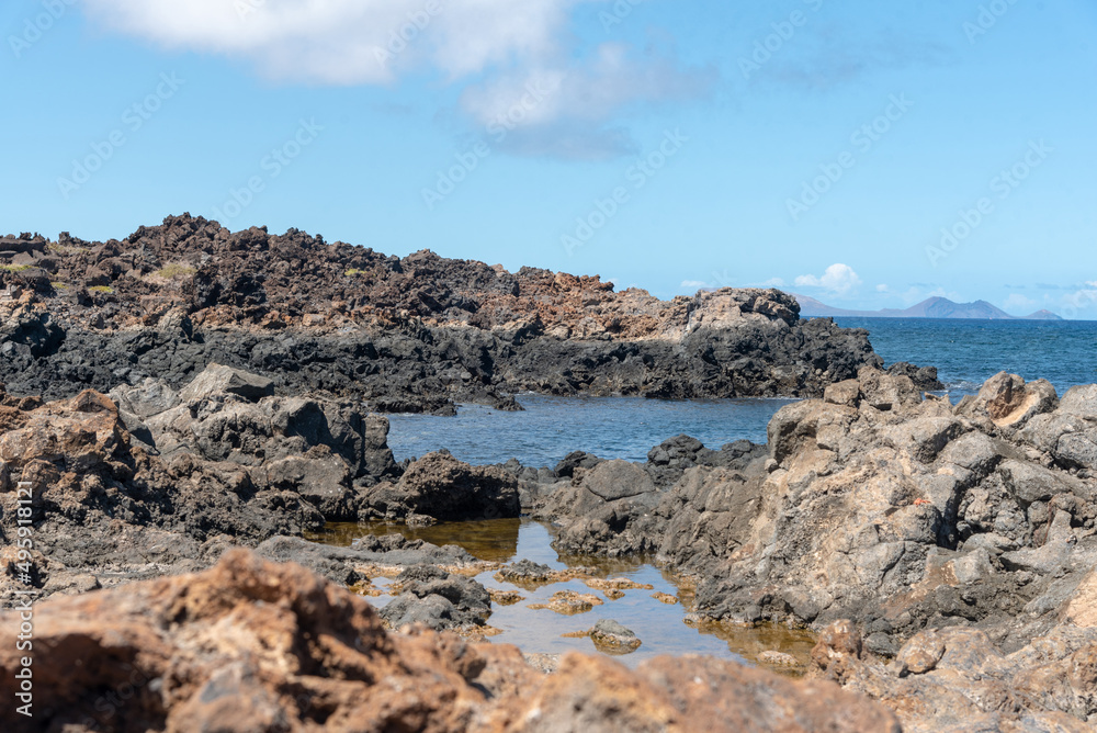 Detalle de la costa de Lanzarote con rocas volcanicas  y lava,  con sus aguas cristalinas durante la marea baja y piscinas naturales de agua marina durante un día soleado en Islas Canarias.
