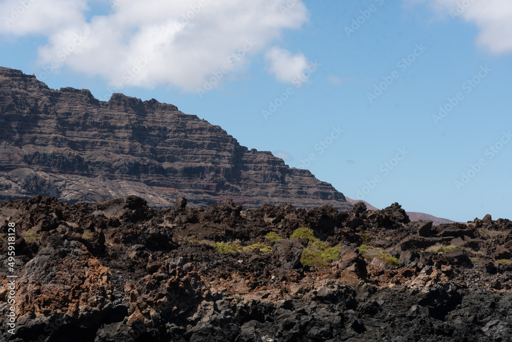 Paisaje volcánico y rocoso de los acantilados de la costa norte de la isla de Lanzarote durante un día soleado con el cielo azul despejado. Recursos naturales de las Islas Canarias.