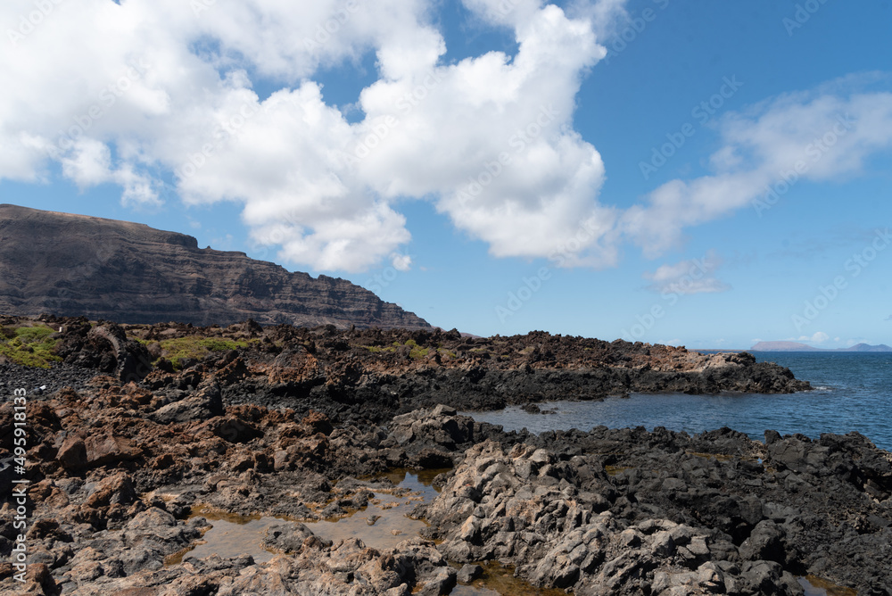 Paisaje rocoso y volcánico de Lanzarote. Vista panorámica de un acantilado con una piscina natural de agua marina en la costa norte durante un día soleado con el cielo azul despejado en Islas Canarias