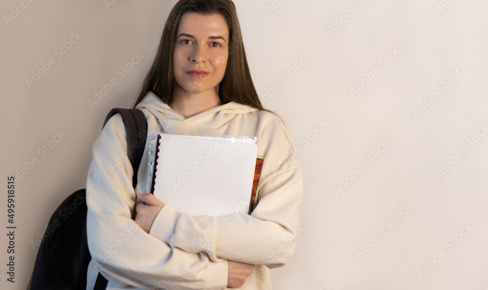 Fototapeta premium Student in trendy sweatshirts standing in hands holds notebooks on wall background with copy space