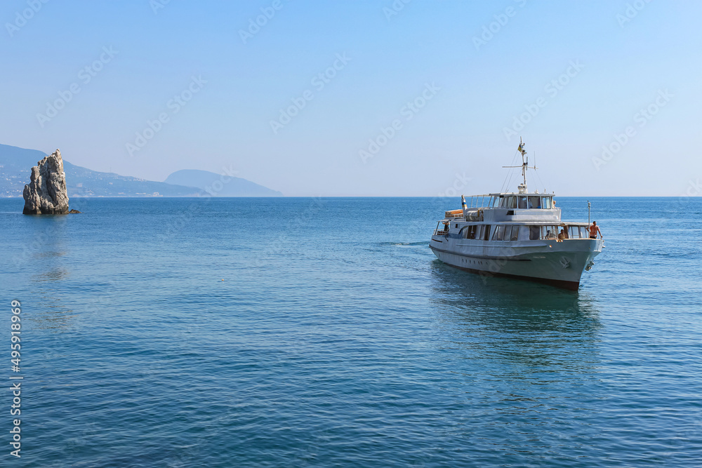 Excursion steamer on a smooth sea surface. The background is a blue sky and mountains. Beautiful seascape. Excursion tourism. Yalta, Crimea.
