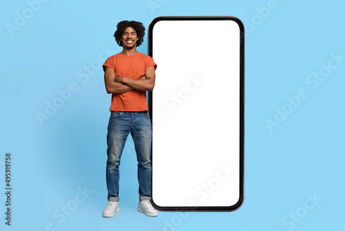 Confident black guy posing by big smartphone with empty screen