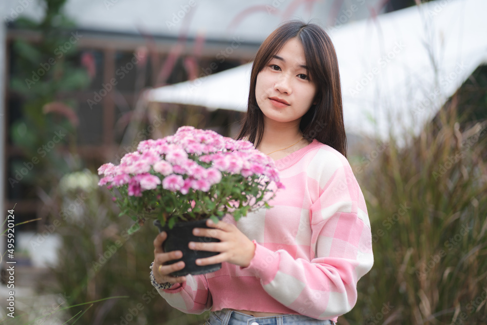 young Asian cute girl wearing pink shirt and holding beautiful pink flower, portrait female model with nature concept with pink flower in hand, happy and smile at outdoor