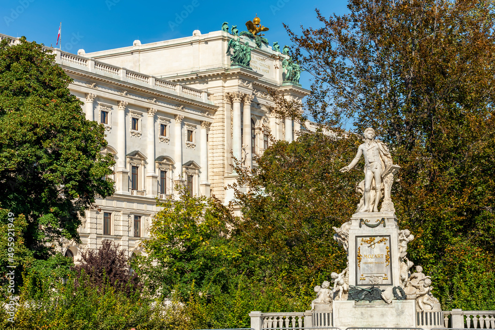 Wolfgang Amadeus Mozart statue in Burggarten park with Hofburg palace at background, Vienna, Austria