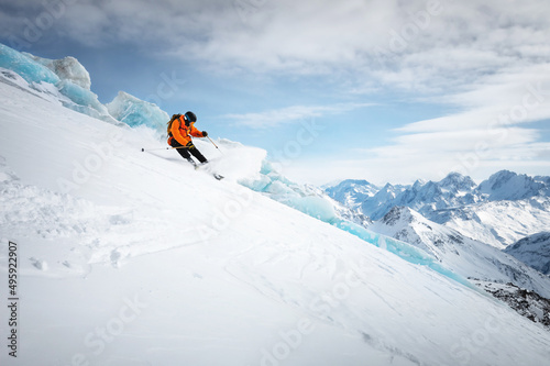 Professional skier ride at speed on a snowy slope against the backdrop of a glacier and high snow-capped mountains on a sunny day. Ski resort space copy presentation