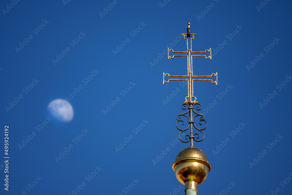 Golden double cross (on Prague Loreta church) and moon on blue sky.